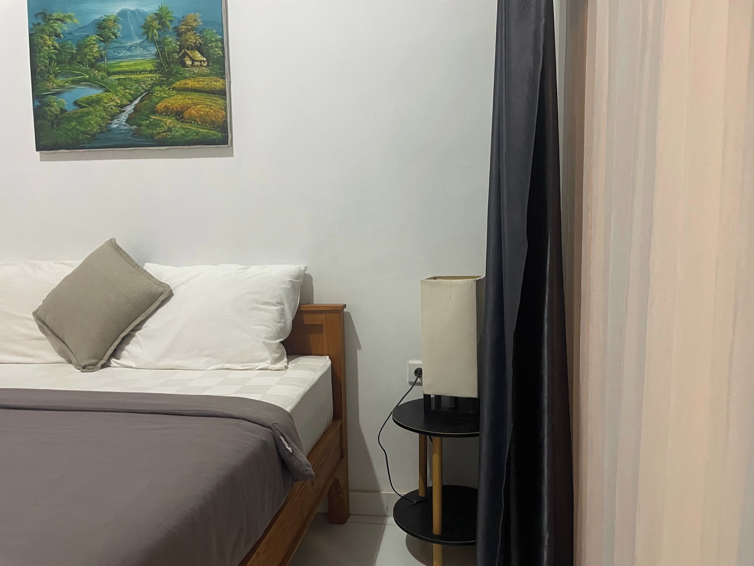 Un dormitorio con una cama, una mesita de noche con una lámpara y un cuadro en la pared.