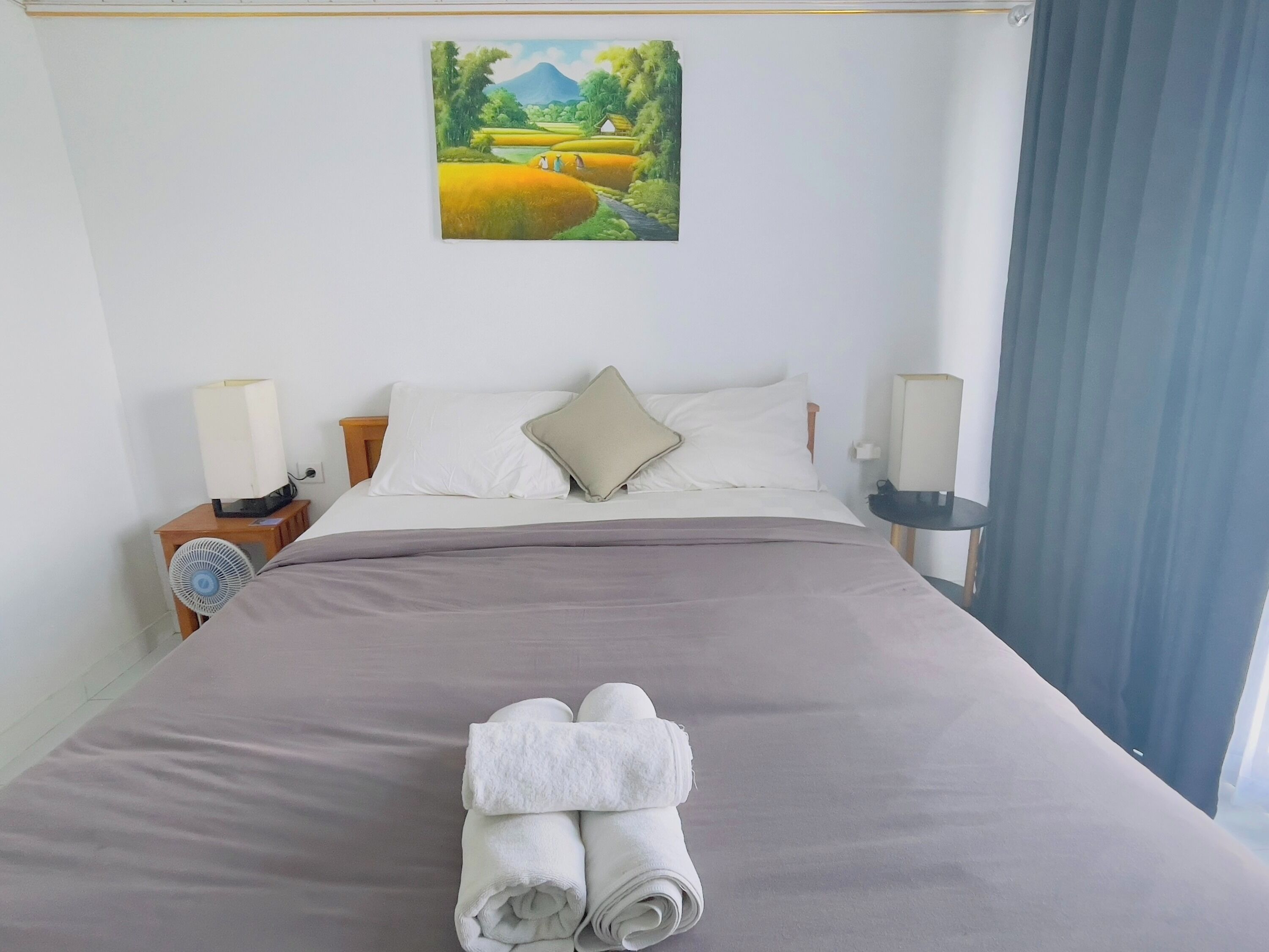Een net opgemaakt bed met een grijze dekbedovertrek, twee kussens en een gevouwen handdoek vooraan.