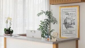 A reception desk with a framed advertisement for a motor inn, a potted plant, and a window with sheer curtains.