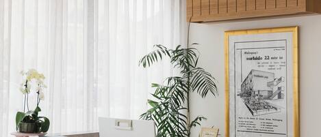 Un comptoir d’accueil orné d’une affiche encadrée faisant la publicité d’un motel, une plante en pot et une fenêtre avec des rideaux légers.