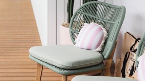 A lounge area with a wicker chair, a cushioned bench, and a cactus plant.