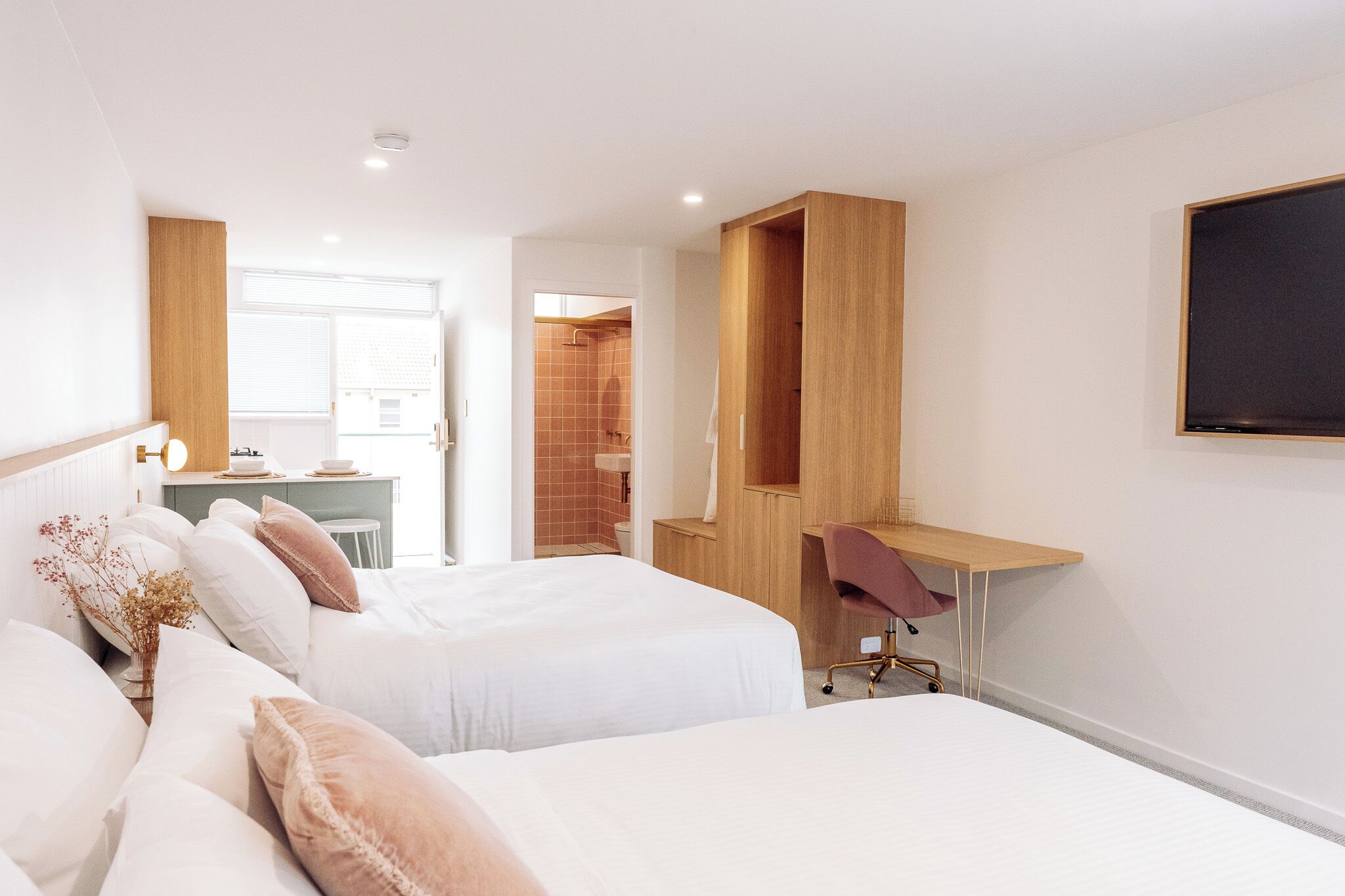 A hotel room with two beds, a desk, and a shower area.