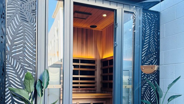 A modern spa entrance with a wooden bench inside, large potted plants, and a blue wall.