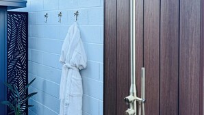 A modern outdoor shower area with a rain shower head, a wooden door, and a white towel hanging on a hook.