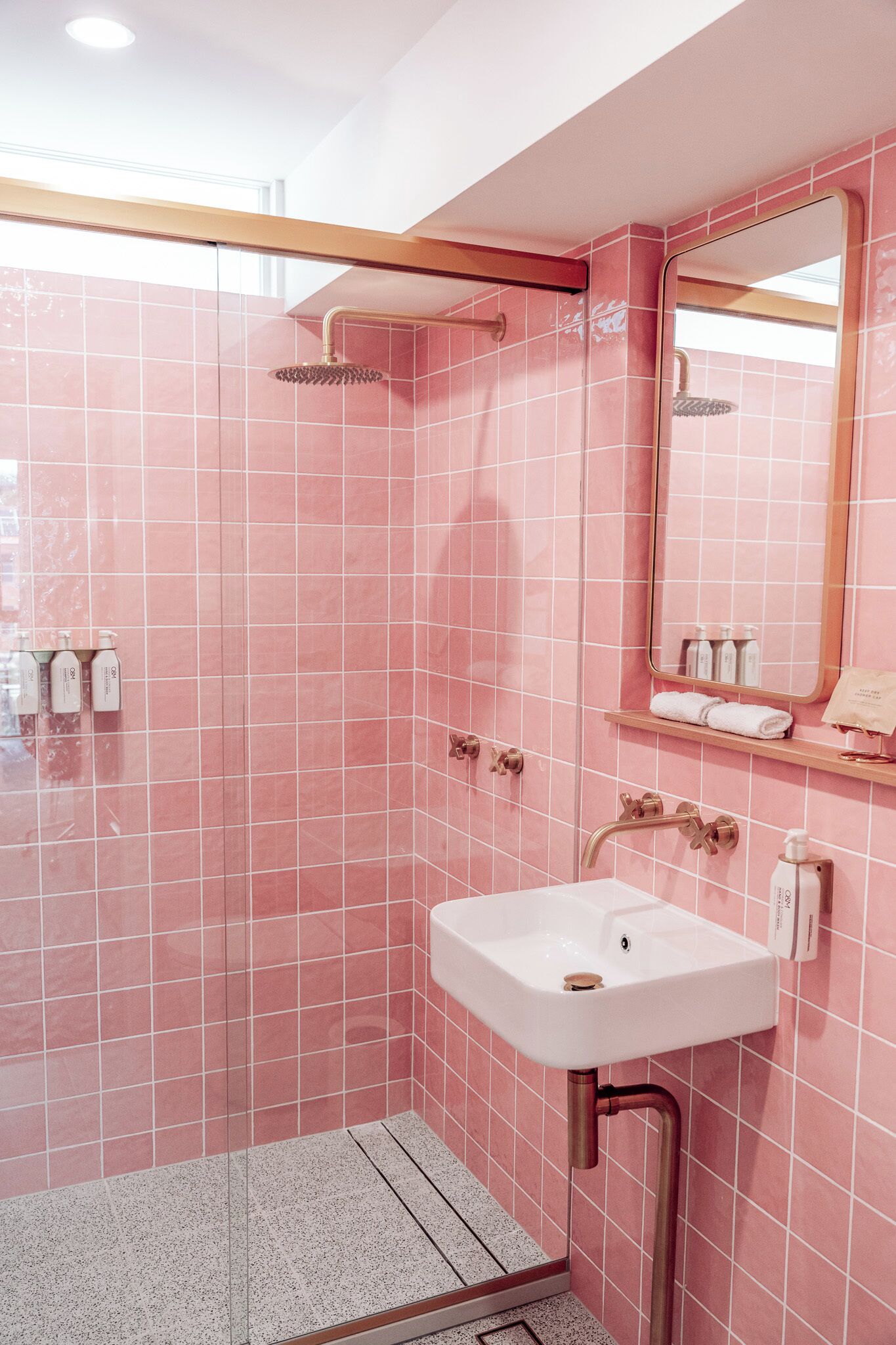 A bathroom with pink tiled walls, a white sink, a showerhead, and a mirror.