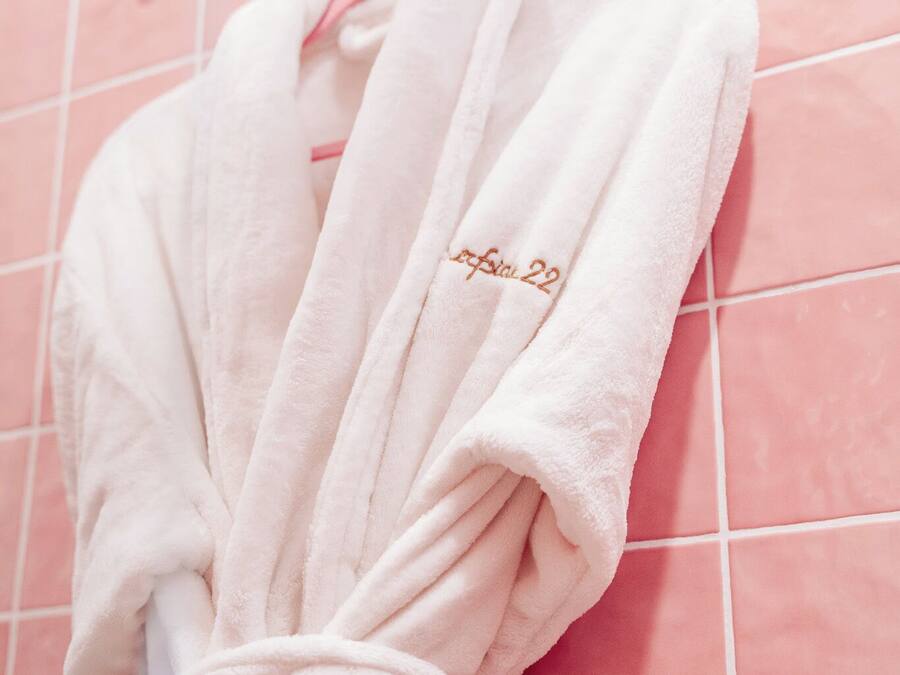 A white bathrobe with a small embroidered text hanging on a pink tiled wall.