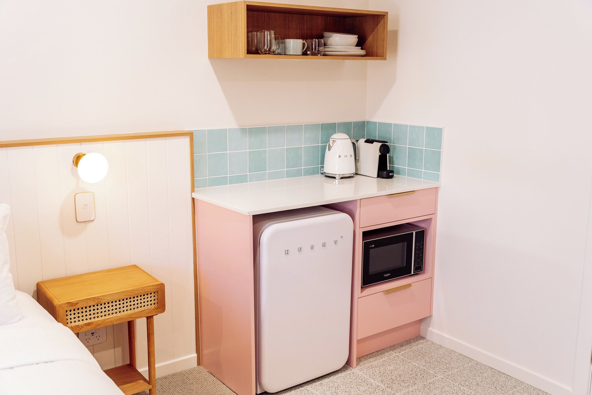 Una kitchenette compacta con un refrigerador blanco, un microondas, un tostador y un estante de madera.