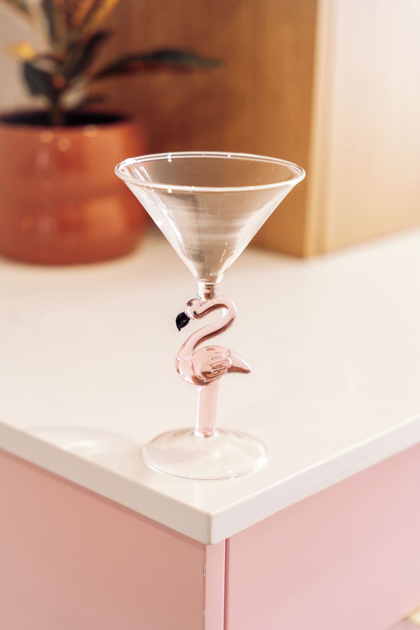 A clear glass martini glass with a pink flamingo design on a white surface.