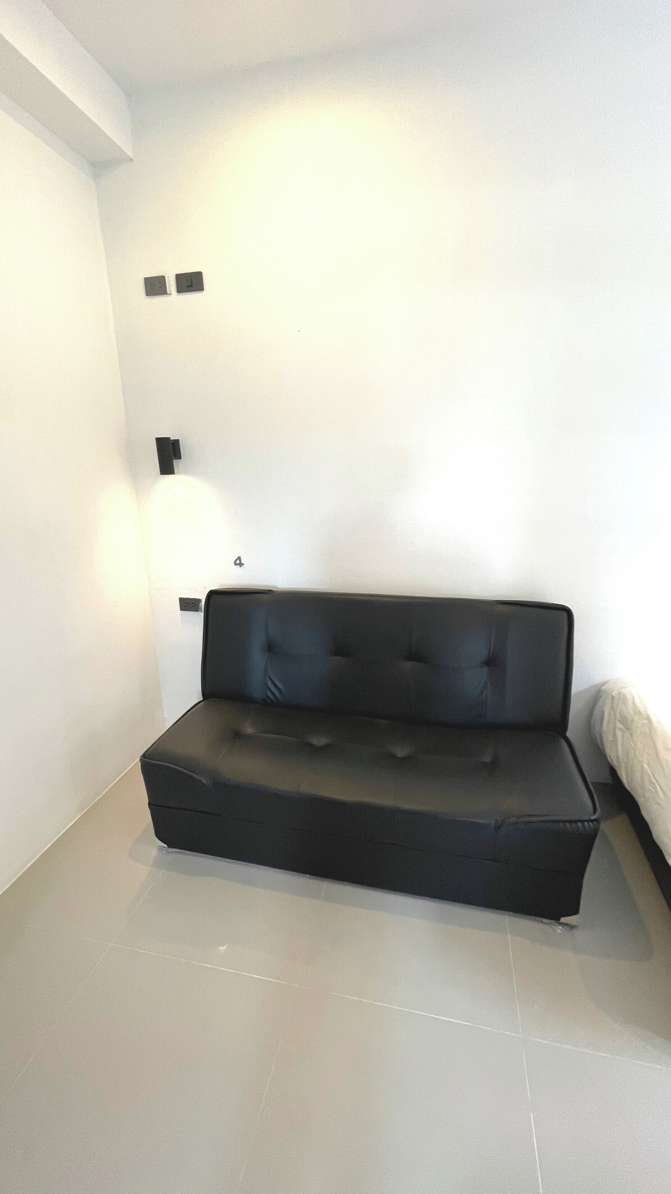 Habitació moderna i minimalista amb un sofà negre, una taula petita i una làmpada penjant de la paret.