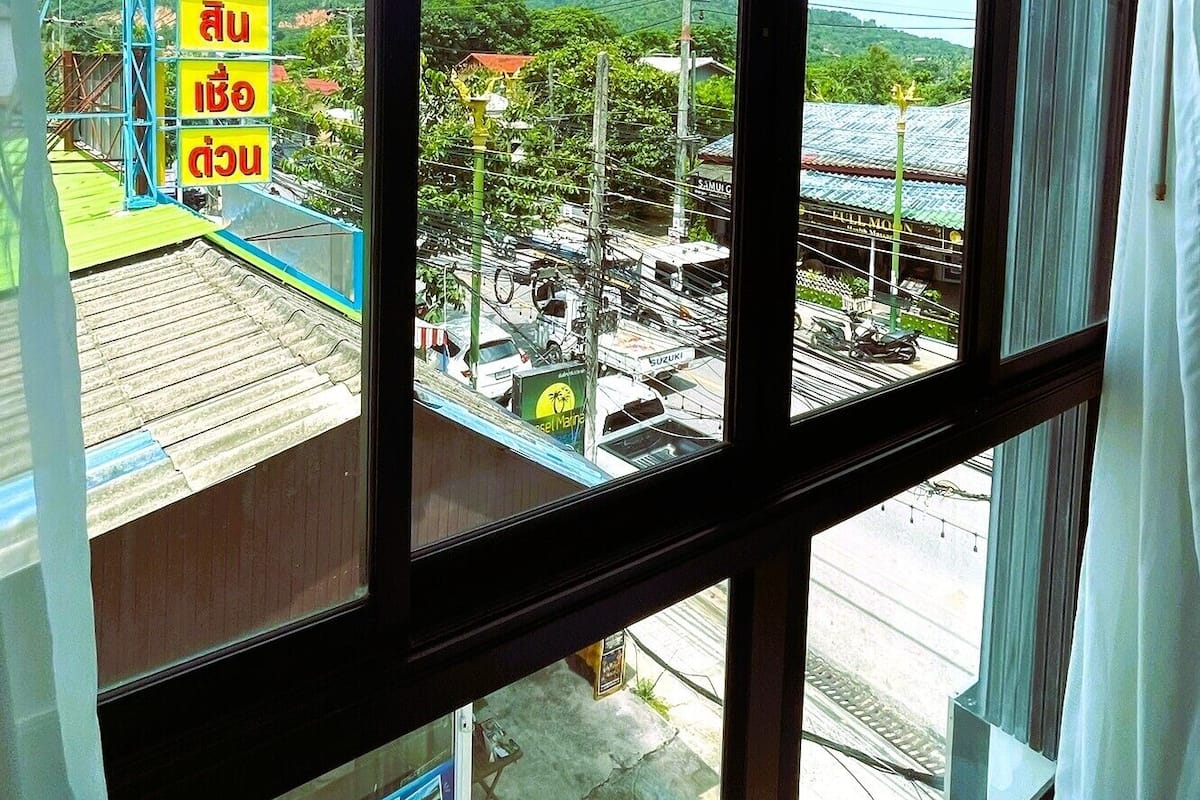 A view from a window with a large glass pane, overlooking a street with a signboard and a building with a red roof.