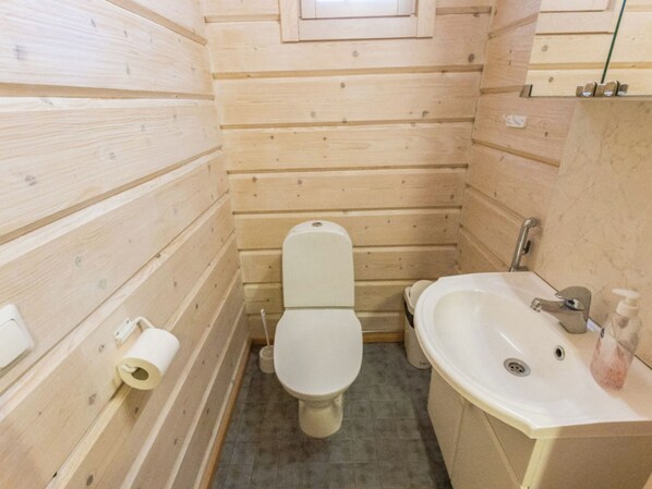 A small, wooden-paneled bathroom with a toilet, sink, and a toilet paper holder.