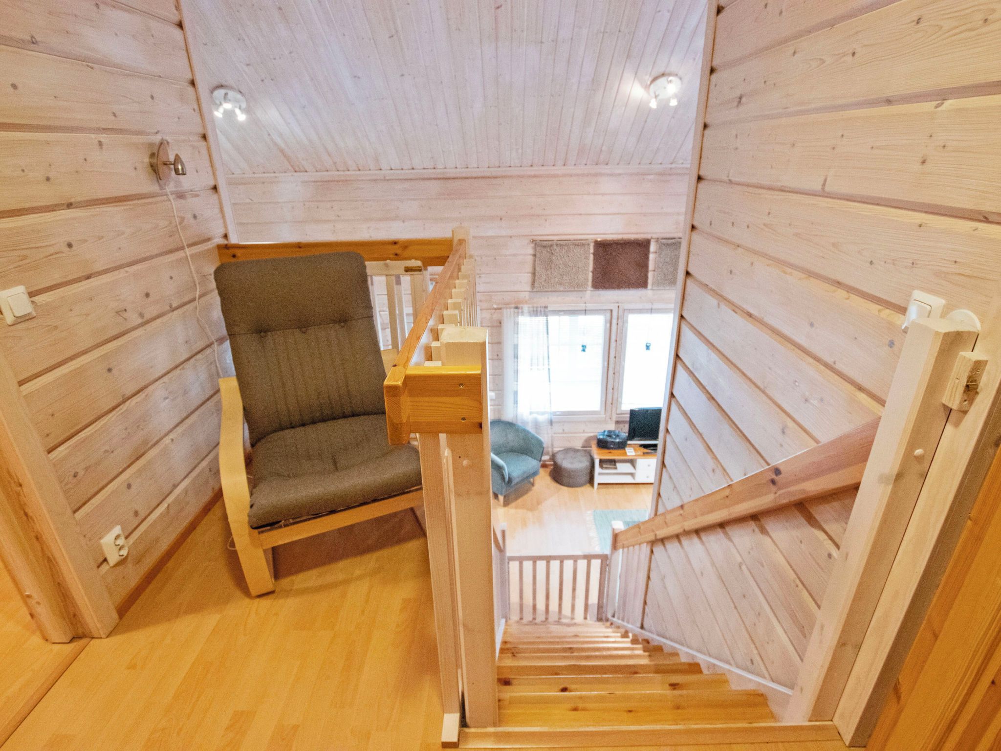 Un interior de madera con una escalera, un sillón acolchado y vista a una sala de estar.
