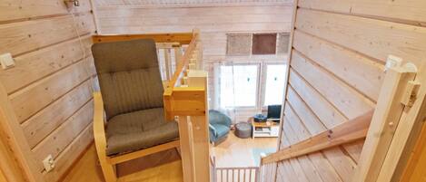 Un interior de madera con una escalera, un sillón acolchado y vista a una sala de estar.