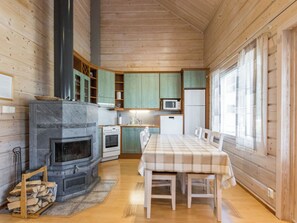 A cozy cabin interior with a wood stove, kitchen area, dining table, and large windows.