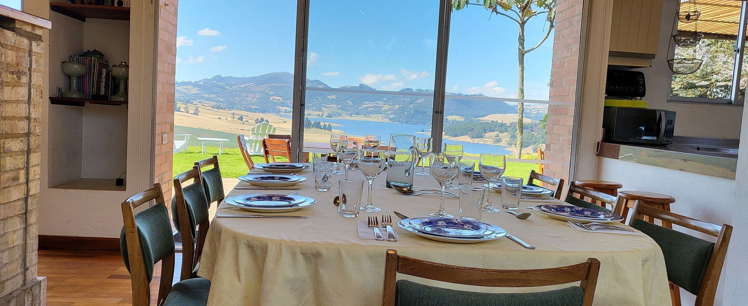 A dining table set for six with a scenic view of hills and a lake.