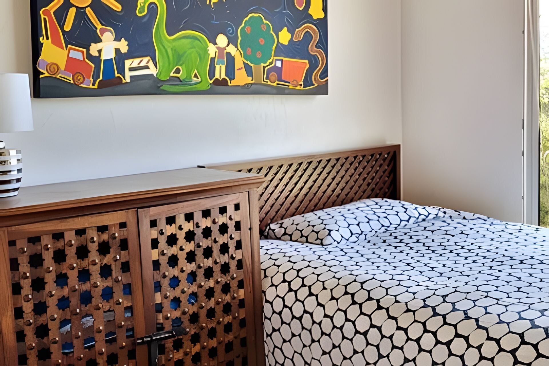 Un dormitorio con una cama que presenta un edredón estampado con motivos geométricos, un cabecero de madera y un armario de madera con diseño de celosía.