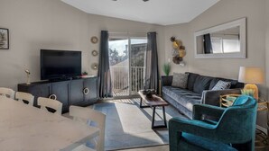 A modern living room with a flat-screen TV, a dining table with chairs, a sofa, and a ceiling fan. - ~VIP by the Beach~ Chair Service Included (Destin)