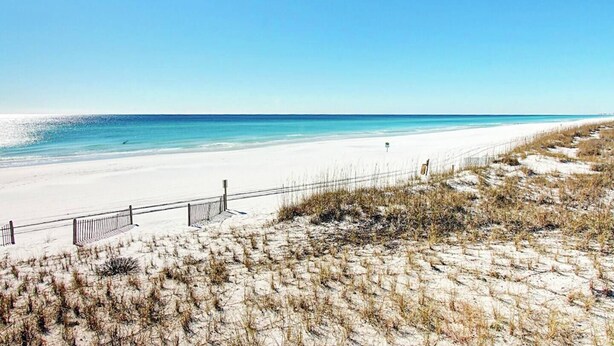 A beach with white sand, a clear blue sky, and a fence along the shore. - ~VIP by the Beach~ Chair Service Included (Destin)