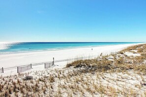 En strand med hvidt sand, blå himmel og et hegn langs kysten.
