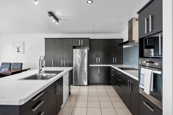 A modern kitchen with stainless steel appliances, dark cabinetry, and a white countertop. - Amazing Lakeview Quite House (Rotorua)