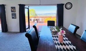 A dining area with a table set for two, a clock on the wall, and a view of a deck with outdoor furniture. - Amazing Lakeview Quite House (Rotorua)