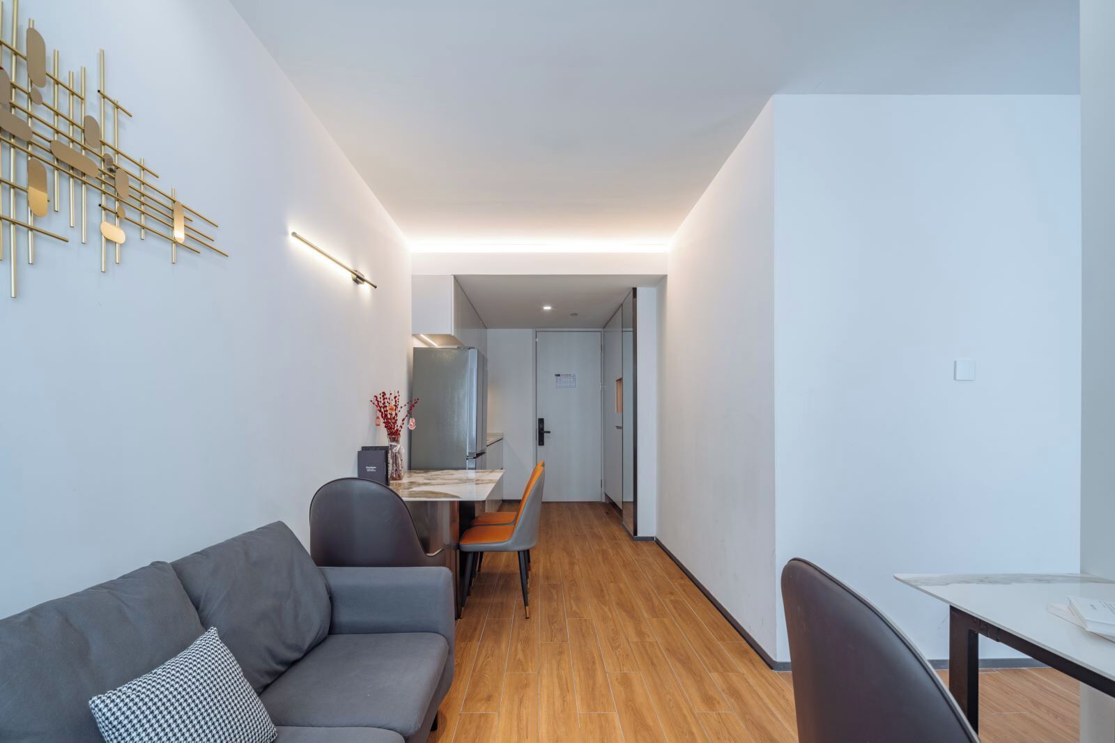 A modern living room with a grey sofa, a dining table with chairs, and a kitchen area in the background.