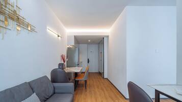 A modern living room with a grey sofa, a dining table with chairs, and a kitchen area in the background.