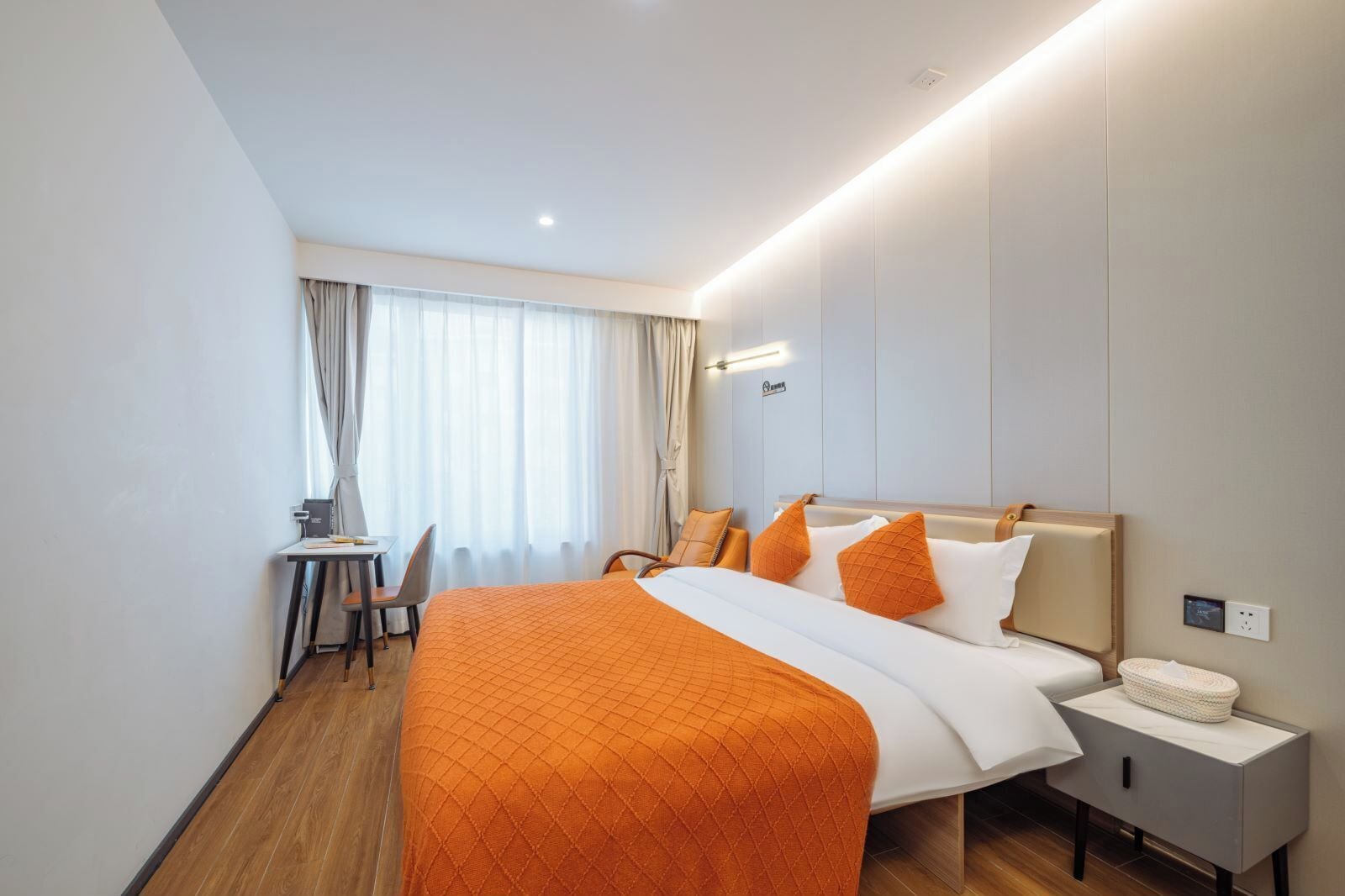 A hotel room with a bed, bedside table, and a desk with a chair.