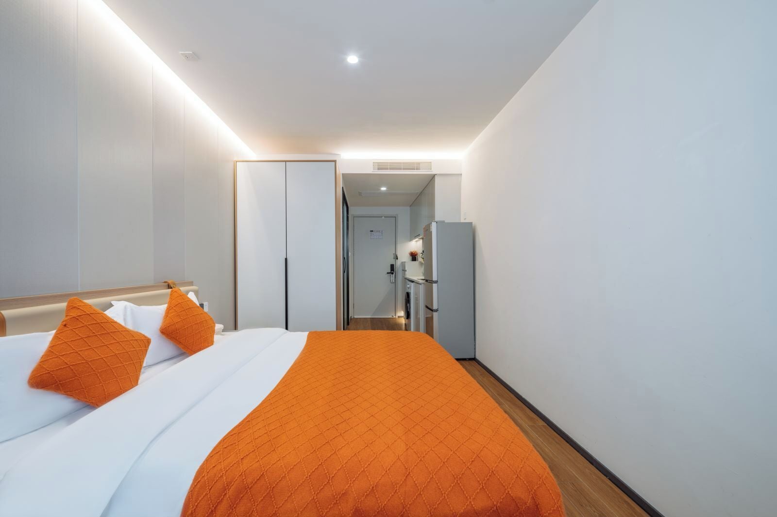 A hotel room with a bed, an orange quilted blanket, and a white pillow.
