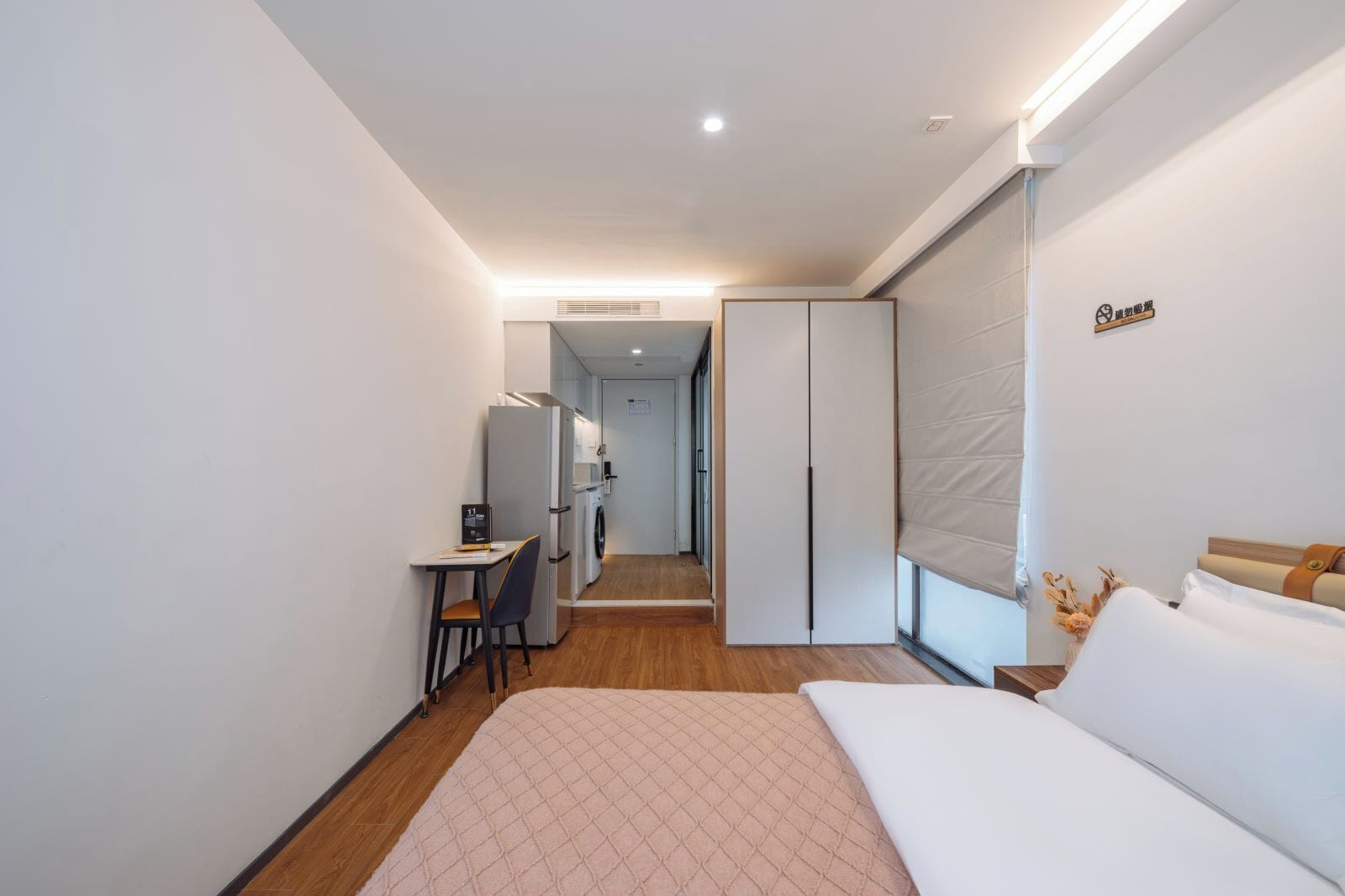 A hotel room with a bed, a desk, a chair, a wardrobe, and a bathroom visible through an open door.