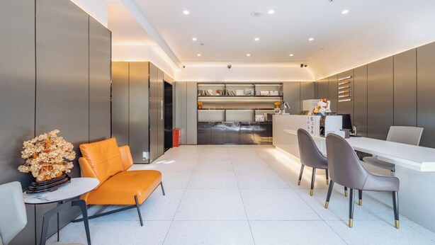 A modern kitchen with built-in appliances, a dining area with a white table and chairs, and a seating area with an orange chair and a vase of dried flowers. - Shanghai Ketangjian Apartment Hotel (Shanghai)