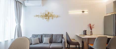 Una sala de estar moderna con un sofá gris, una mesa de comedor y sillas. Hay un aire acondicionado instalado en la pared y un accesorio de iluminación decorativo.
