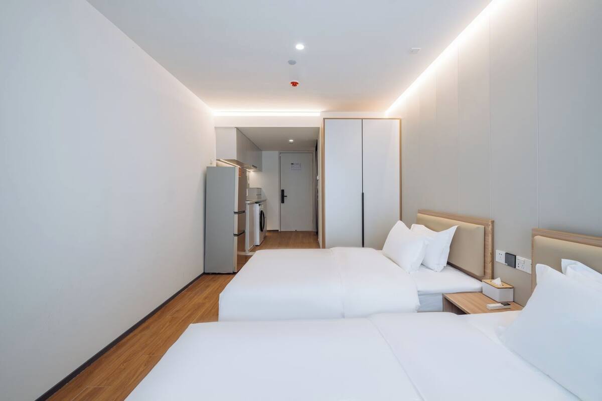 A hotel room with two beds, a wardrobe, a small table, and a washing machine in the background.