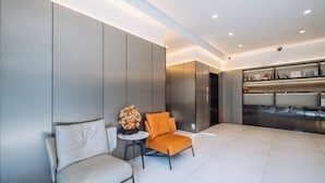 A modern waiting area with a white sofa, an orange chair, and a small table with a decorative vase. - Shanghai Ketangjian Apartment Hotel (Shanghai)