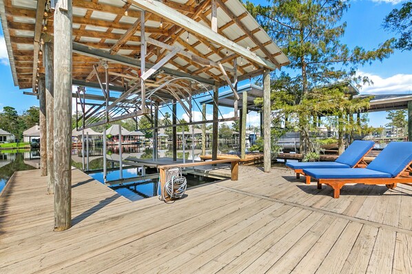 A wooden deck with a pool, lounge chairs, and a covered area with a view of the water.