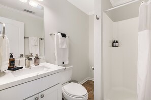 A bathroom with a white sink, mirror, and toilet. There are two bottles of hand soap on the sink.