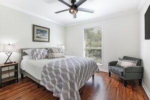 A bedroom with a bed, a chair, a nightstand, a ceiling fan, and a window with blinds.