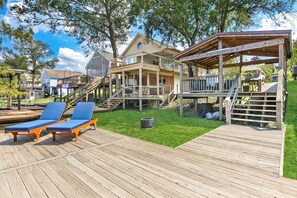 A wooden deck with two blue lounge chairs, a covered wooden deck area, and a house with a porch and stairs leading to a deck.