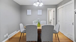 A dining area with a wooden table, four grey chairs, a green vase with flowers, and a chandelier.