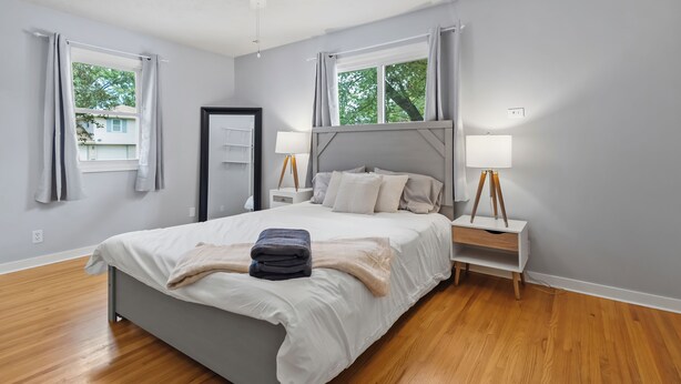 A bedroom with a bed, bedside lamps, a ceiling fan, and a window with curtains.