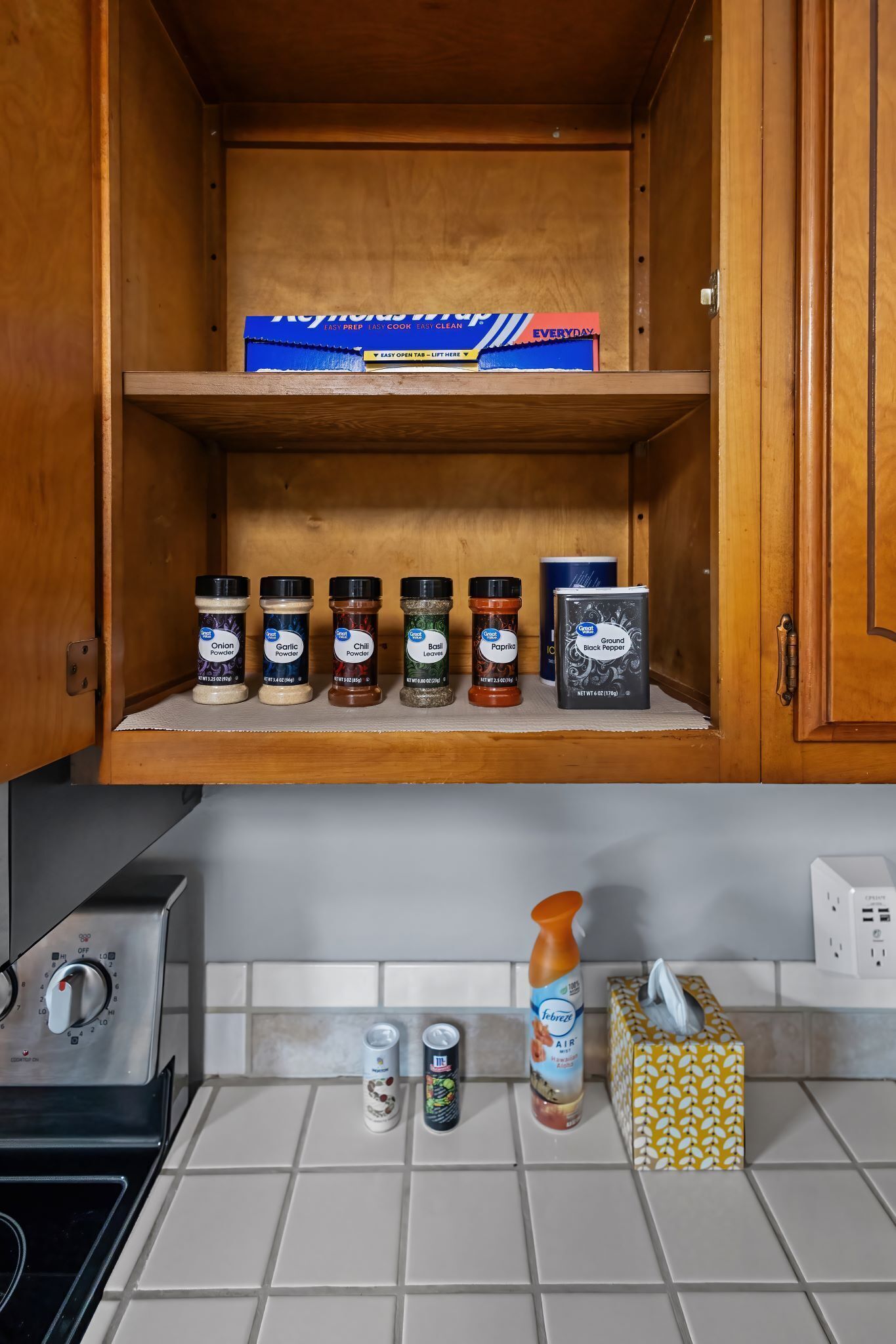A kitchen with a wooden cabinet containing spice jars and a box of paper towels.