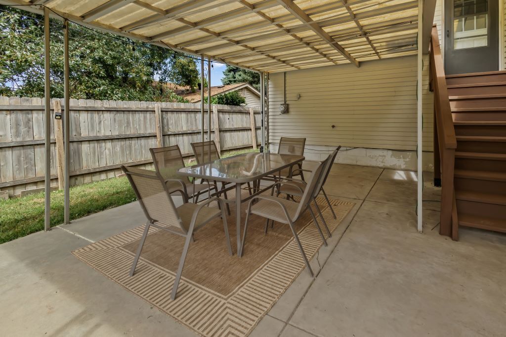 An outdoor patio with a table and chairs, a covered area, and a wooden fence in the background.