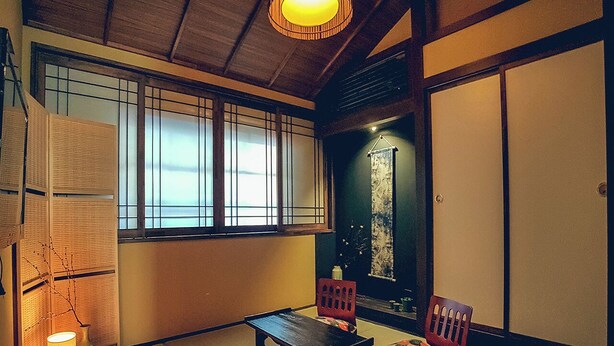A traditional Japanese room with tatami flooring, a low table, two chairs, a hanging scroll, and a window with shoji screens. - Tainan Kyomachiya Emoh House (Tainan)