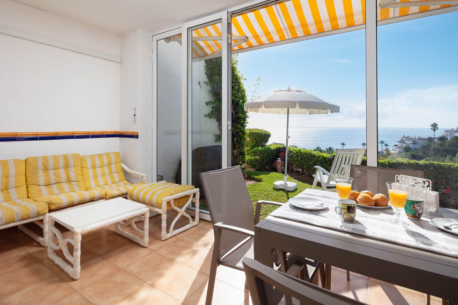 A balcony with a sofa, chairs, and a table set for breakfast.