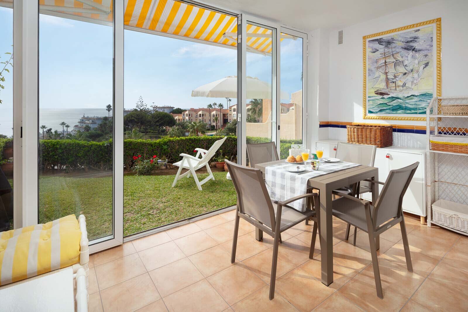 A dining area with a table set for two, a white chair, and a view of the sea through large sliding glass doors.