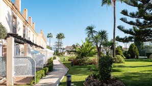Un camino que lleva a un edificio con fachada blanca y balcones, rodeado de céspedes cuidados y palmeras.