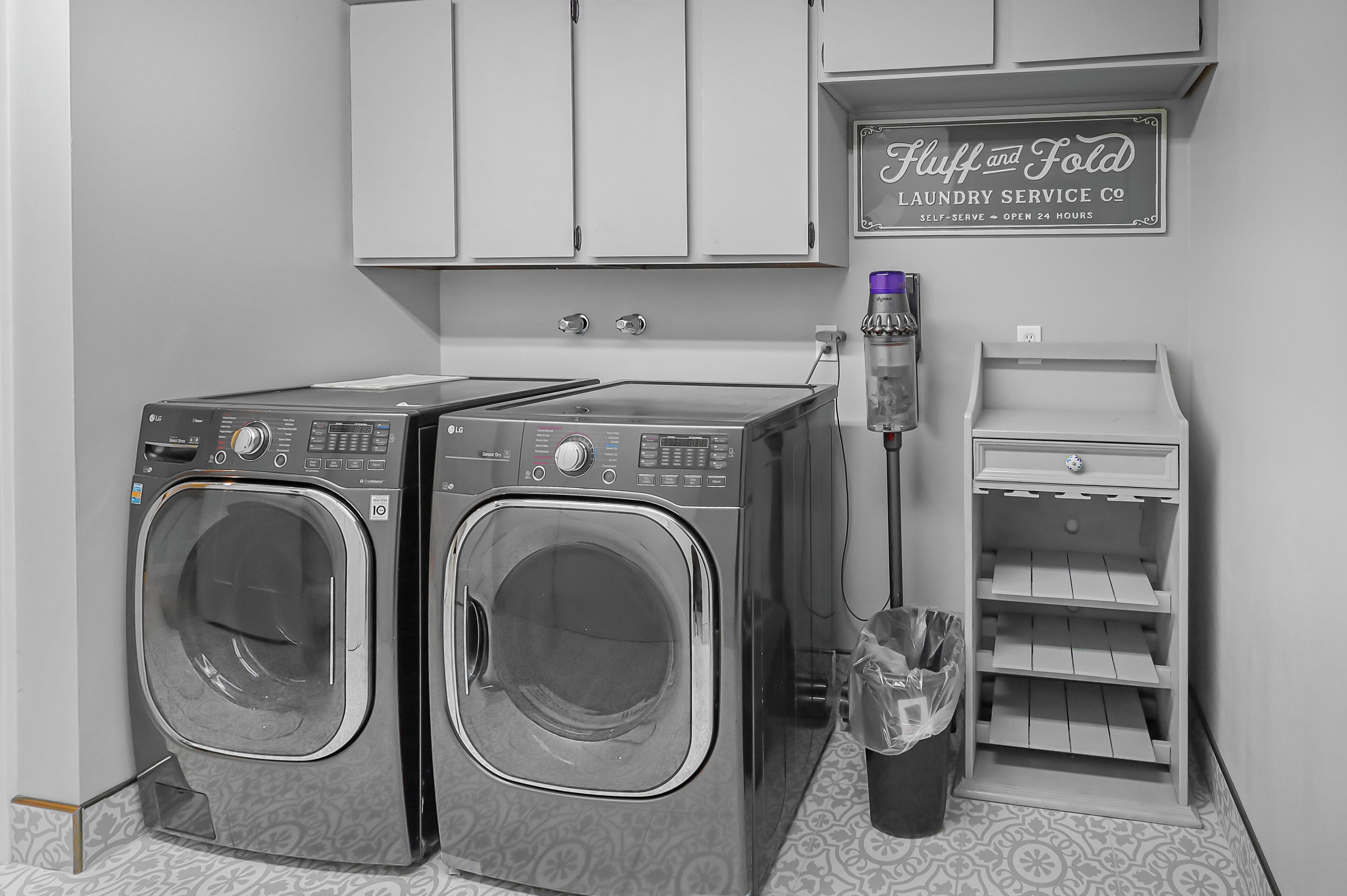 Une buanderie équipée de deux lave-linge LG à chargement frontal, d’un aspirateur Dyson et d’un panneau indiquant qu’il s’agit d’une laverie en libre-service.