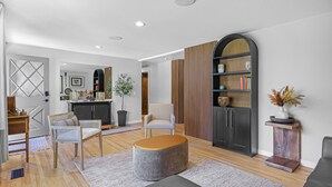 Un salon moderne avec un pouf gris, un fauteuil blanc et une bibliothèque en bois.