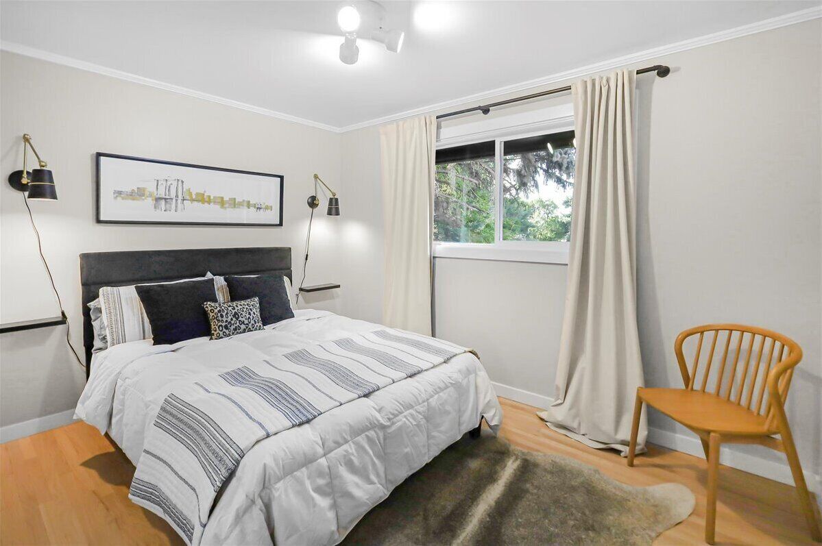 Une chambre à coucher comprenant un lit, une chaise, une fenêtre avec des rideaux et deux lampes fixées au mur.