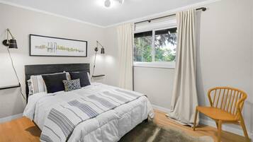 Une chambre à coucher comprenant un lit, une chaise, une fenêtre avec des rideaux et deux lampes fixées au mur.